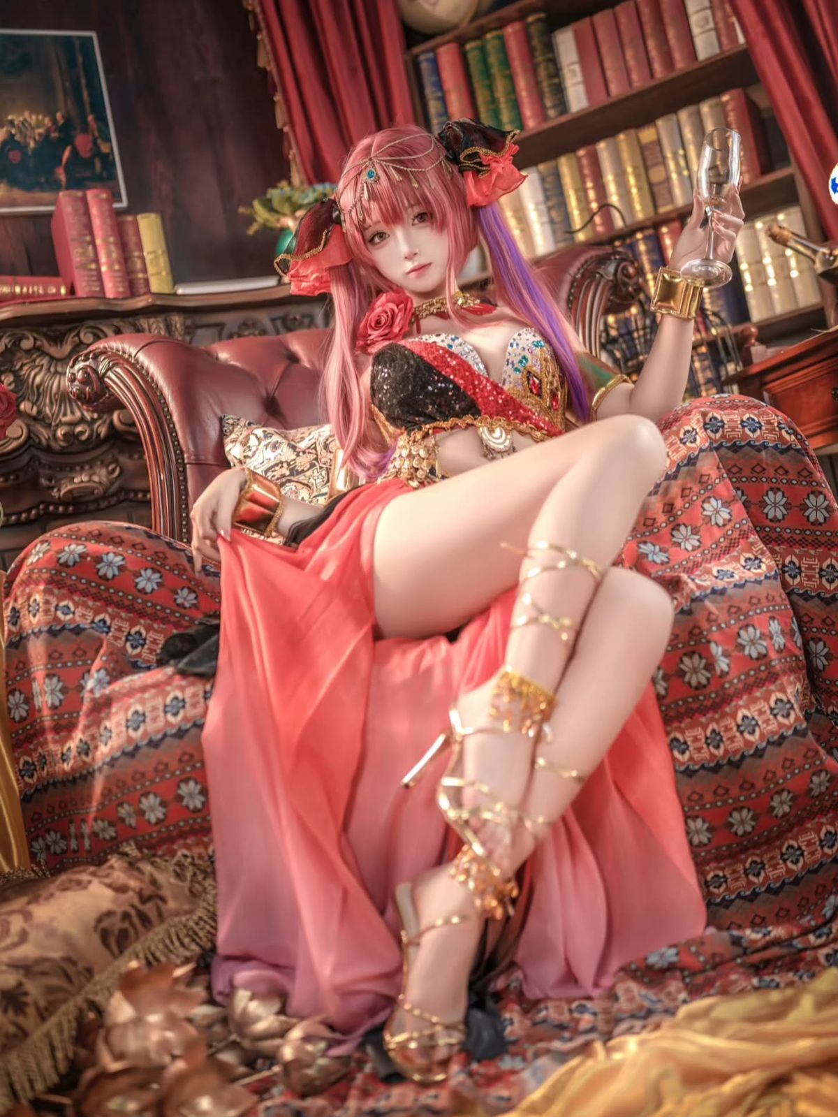Pink-haired cosplay character in an ornate red costume, seated in a richly decorated library